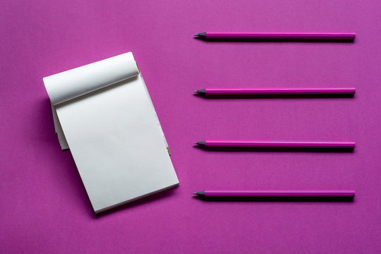 Top view notepad with pencils and copy space on pink paper background.