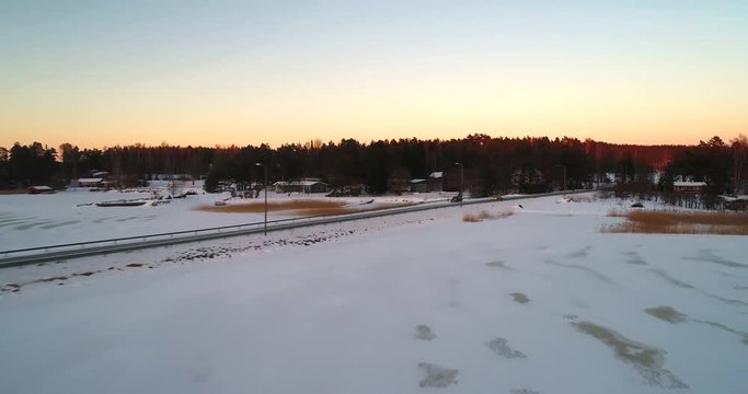 Car on a winter bridge, Cinema 4k aerial view following a yellow suv car on a frozen archipelago bridge, on a sunny winter evening dawn, in sarkisalo, Varsinais-suomi, Finland