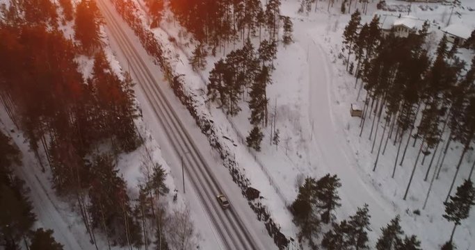 Car on a winter road, Cinema 4k aerial view following car on a frozen archipelago route, revealing the sunset above a town, in sarkisalo, Varsinais-suomi, Finland