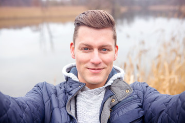 selfie of handsome blond man in front of lake