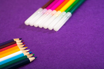 Fototapeta premium Seven multicolored felt pens and nine different colored pencils on a purple felt background with space for text. Back to school. Art lessons.