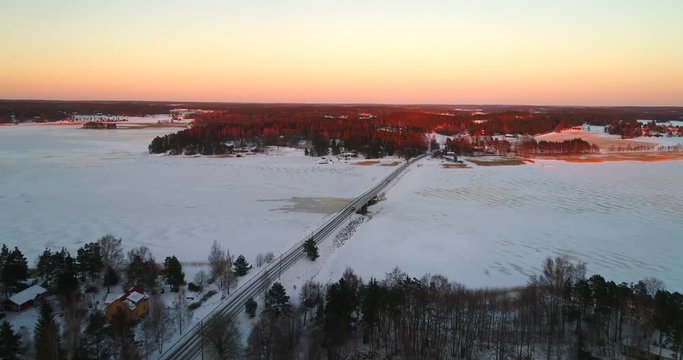Car on a winter road, Cinema 4k aerial view following cars on a frozen archipelago bridge, on a sunny winter evening dawn, in sarkisalo, Varsinais-suomi, Finland
