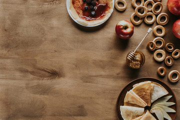 top view of tasty pancakes with apples, berries, honey and bagels on wooden table