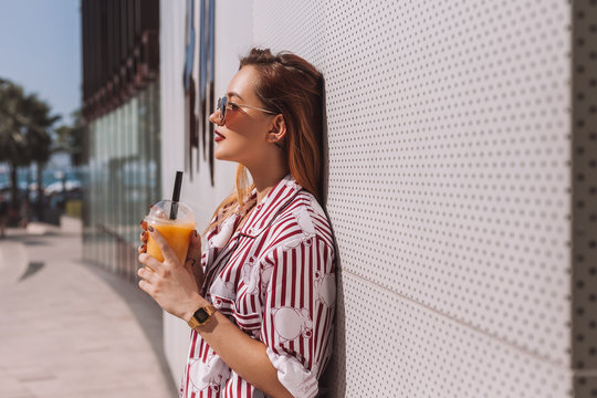 Side View Of Attractive Young Woman With Cocktail In Plastic Cup Leaning Back On Wall