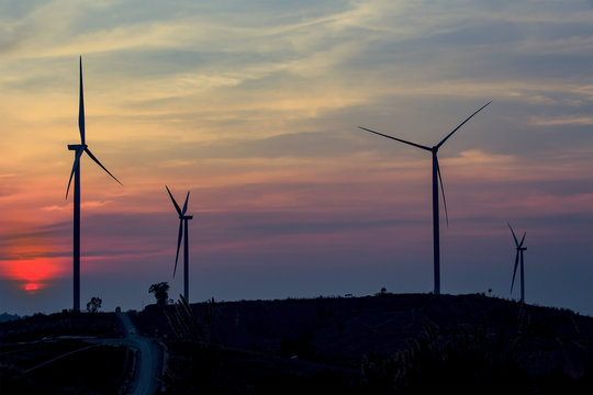 Silhouette wind turbine farm over moutain with orange sunset and cloud in blue twilight sky