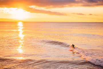 Surfer in ocean at bright sunset or sunrise. Winter surfing in sea