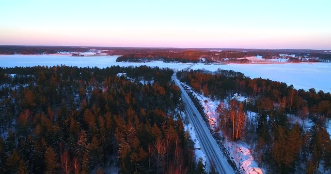 Car on a winter road, Cinema 4k aerial view following cars, above a frozen archipelago route, at a evening sunset dawn, in sarkisalo, Varsinais-suomi, Finland