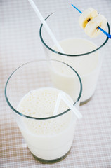 Frothy banana milkshake served in two glasses with drinking straw  decorated with banana slices