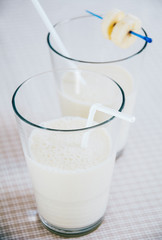 Frothy banana milkshake served in two glasses with drinking straw  decorated with banana slices