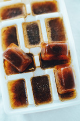 Ice cubes made with coffee in ice cube tray to prepare refreshing coffee drinks. Close up on white background, soft focus.