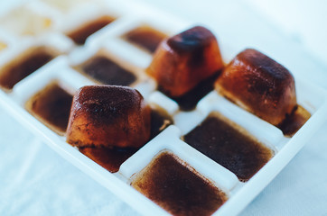 Ice cubes made with coffee in ice cube tray to prepare refreshing coffee drinks, close up on white...