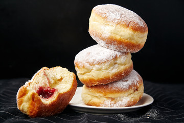 A stack of three sufganiyot donuts with jelly on black background