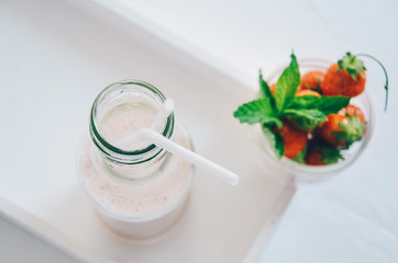 Strawberry milkshake in glass bottle with drinking straw garnished with fresh strawberries on white background