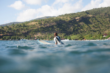 Naklejka premium sportswoman swimming on surf board in ocean, coastline on background