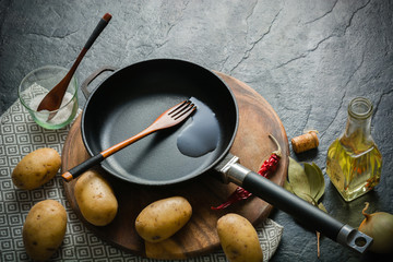 Cast-iron frying pan and potatoes. Cooking fried food. Dark stone background.