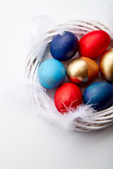 Eggs painted in various colors arranged with feathers in twig wreath on white background. Easter traditions concept.