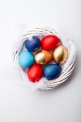 Eggs painted in various colors arranged with feathers in twig wreath on white background. Easter traditions concept.
