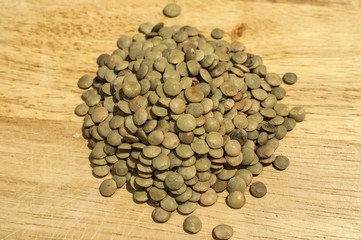Pile of bulk dried organic lentil seeds closeup on wooden board background