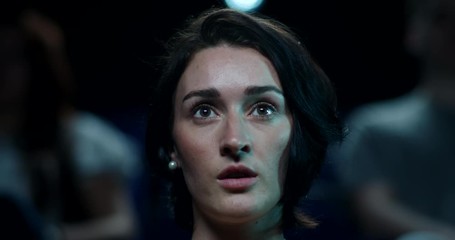 A woman reacts impressed to a moment in a film while at the cinema