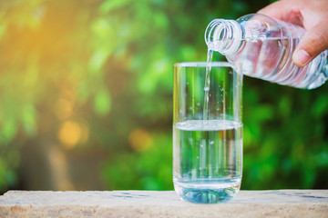 People are pouring water from a plastic bottle into a glass of water.