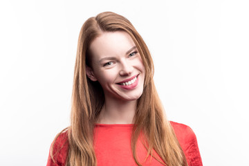 Delicate beauty. The portrait of a pretty ginger-haired woman in a red t-shirt smiling at the camera and tilting her head while posing isolated on a white background