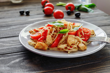 Italian pasta with chicken, tomatoes, red pepper,basil in a plate n a wooden table