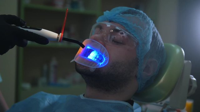 Doctor and patient with lip dilator in the dental office, cleaning with ultraviolet light and orange protective screen