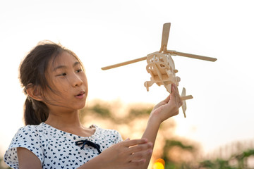 Girl holding helicopter wooden plane toy with sun set.