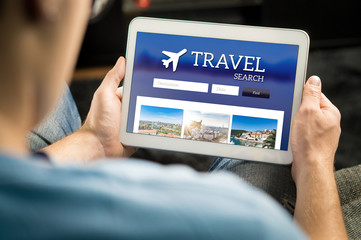 Man searching cheap flights, hotel or holiday package on internet by using online travel search application with tablet. Ordering holiday and making reservation on website with smart device.