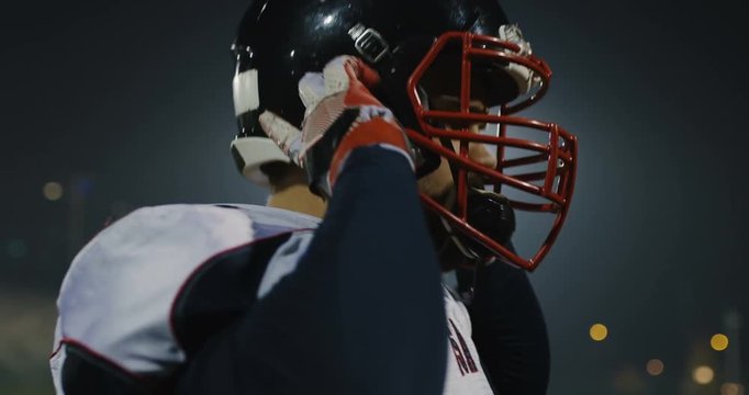 American football player putting on his protective helmet against bright stadium illumination lights