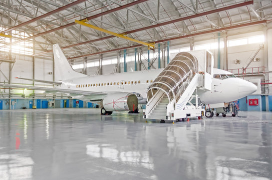 Passenger airplane in the hangar, enclosed engines and gangway at the entrance to the aircraft.