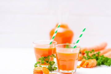 Carrot juice in beautiful glasses, cut orange vegetables and green parsley on white wooden background. Fresh orange drink. Close up photography. Selective focus. Horizontal banner