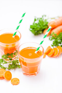 Carrot juice in beautiful glasses, cut orange vegetables and green parsley on white wooden background. Fresh orange drink. Close up photography. Selective focus. Vertical banner