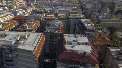 Aerial view of a group of buildings in the Tuscolana district in Rome, Italy. The roofs are passable and with antennas and TV. down the sunlit streets there are cars and trees.