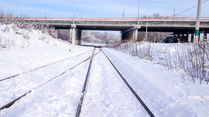 An automobile bridge across the railway crossing. Sleepers from the train, electric train in the city in the winter. They are covered with snow from a storm. The road going into the distance.