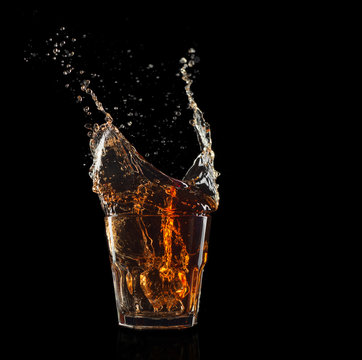 Glass of whiskey with splash isolated on black background