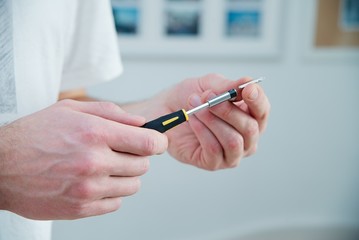 Man holds a screwdriver in his hands - white skin, black and yellow screwdriver. Master works at home