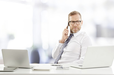 Businessman consulting on mobile phone with his client. Portrait of happy financial assistant business man using cell phone and making call while working on laptop at the office. 