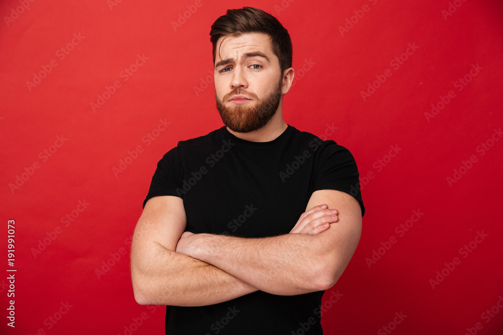 Canvas Prints Portrait of muscular serious man 30s wearing black t-shirt posing on camera with hands crossed, isolated over red background