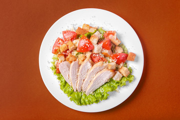 Caesar salad with chicken, tomatoes, breadcrumbs, cheese top, decorated with lettuce leaves on a monophonic background. View from above