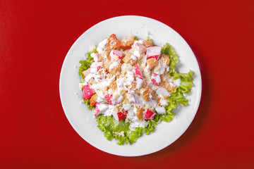 Fototapeta na wymiar Salad with crab meat, breadcrumbs on a monophonic red background. It is decorated with lettuce leaves. View from above