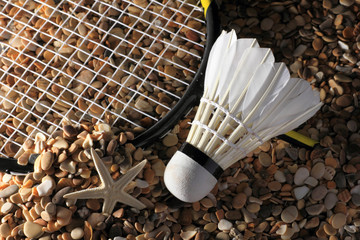 Set Badminton racket and shuttlecock feathers on rocks, beach background.