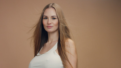 Fototapeta premium beauty woman model in studio on beige background with wind in hair bllowing it. white top