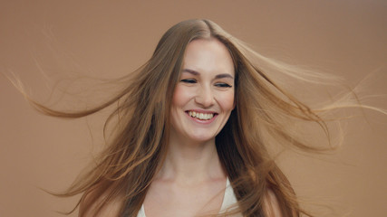 Fototapeta premium beauty woman model in studio on beige background with wind in hair bllowing it lauging a lot