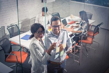 High angle view of business people working near glass wall with sticky notes.