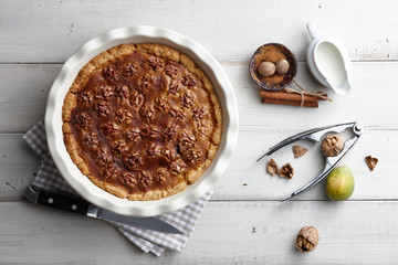 Traditional walnut pie with nuts and nutcracker on white wooden planks, top view