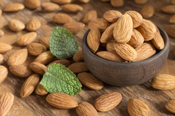 Almonds in a black bowl against dark rustic wooden background - Prunus dulcis