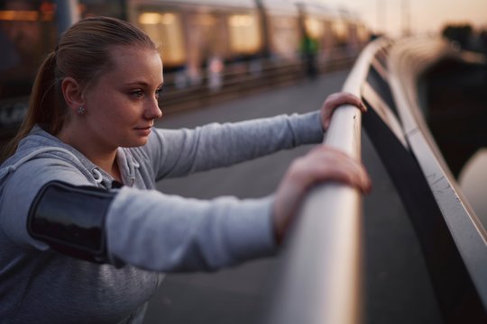 Curvaceous young woman training, leaning against footbridge handrail at dusk