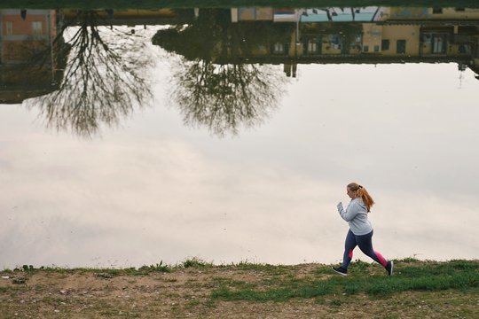 Curvaceous young female runner running on riverside
