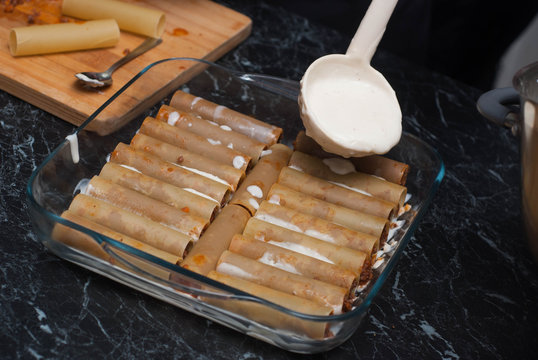 Uncooked Cannelloni Pasta In Glass Bowl With Bechamelle Sauce. Pouring White Saunce Over Cannelloni. Food Preparing Proces. Italian Cuisine.